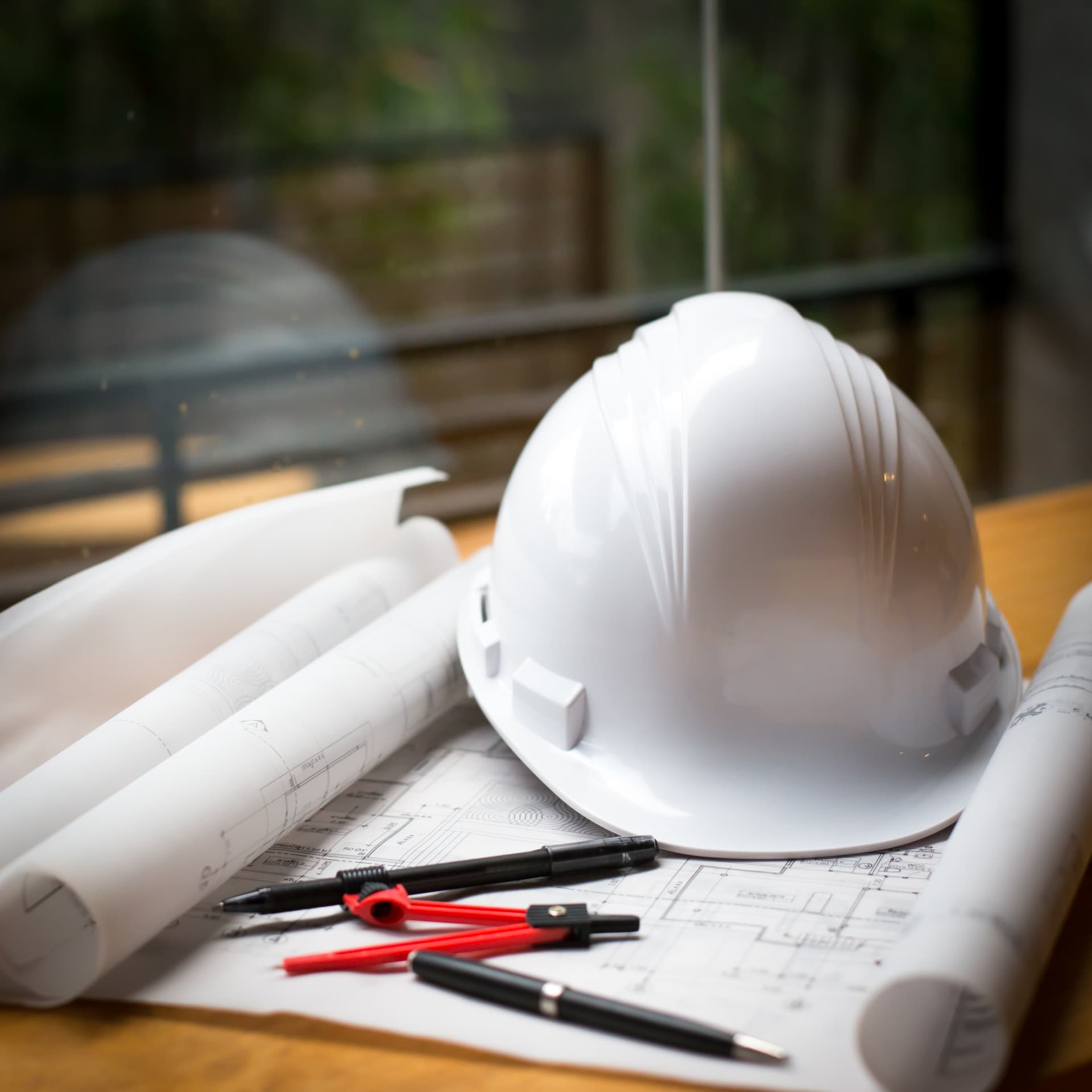Capacete de segurança branco sobre projetos enrolados em mesa de trabalho