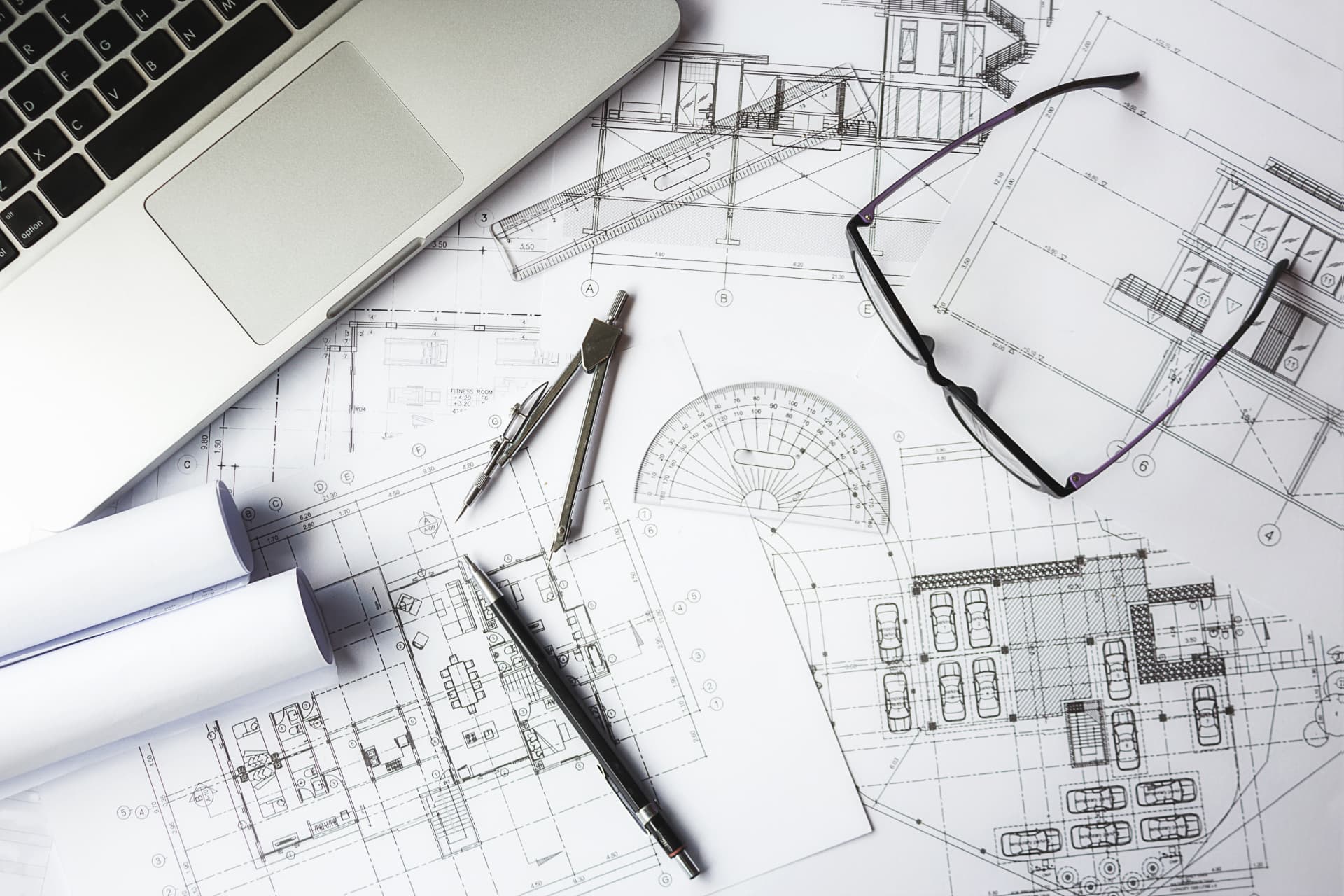 Notebook, óculos e plantas de arquitetura sobre a mesa